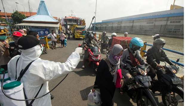 An officer sprays disinfectant on passengers who arrived at a port amid the spread of coronavirus disease in Surabaya, East Java province, Indonesia
