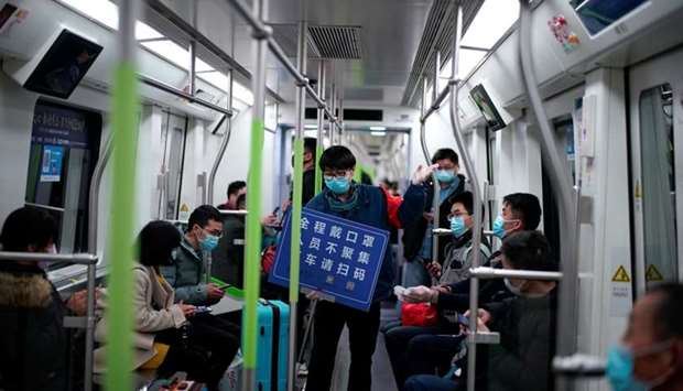 A staff member wearing a face mask holds a placard while standing among passengers on a subway train, on the first day the city's subway services resumed following the novel coronavirus disease (Covid-19) outbreak, in Wuhan of Hubei province, the epicentre of China's coronavirus outbreak.