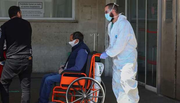 A healthcare worker wearing a protective face mask and suit pushes a patient in a wheelchair near the emergency unit at 12 de Octubre hospital during the coronavirus disease (Covid-19) outbreak in Madrid,
