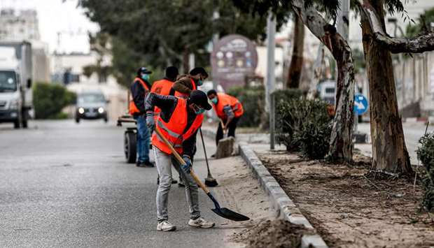 Mask-clad workers clean up a street in Gaza City, yesterday, during lockdown amidst measures to contain the Covid-19 coronavirus pandemic.