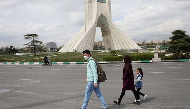 A family wears protective face masks and gloves, amid fear of coronavirus disease as they walk by the iconic Freedom Square, in Tehran, Iran.