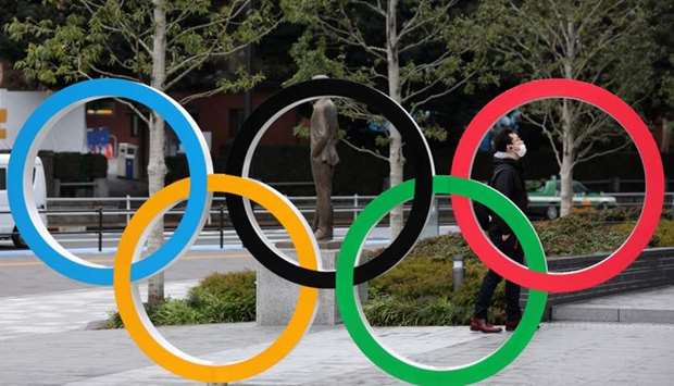 A man wearing protective face mask, following the outbreak of the coronavirus, is seen through The Olympic rings in front of the Japan Olympics Museum in Tokyo