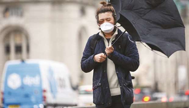 A man wearing a protective face mask walks with an umbrella in London yesterday.
