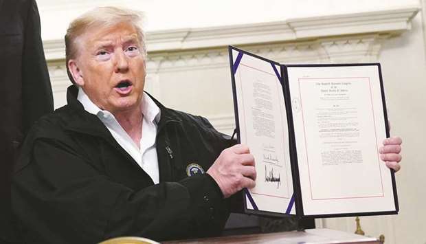 Trump holds up the $8.3bn emergency funding bill to combat Covid-19 after signing it in the Diplomatic Room of the White House in Washington, DC.