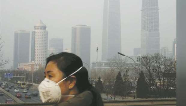 A woman wearing a protective mask makes her way in a business district on a heavily polluted day in Beijing. China, which spews more carbon into the atmosphere than the US and European Union combined, is being forced to give greater priority to an economy that had wilted during the trade war with Washington and is now being flattened by the coronavirus epidemic.