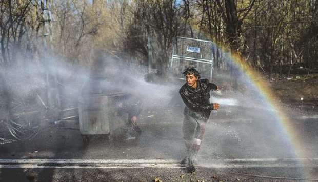 A migrant runs as another one takes cover behind a trash container as Greek police personnel use water cannons to stop them from breaching fences in the Turkey-Greece border province of Edirne.