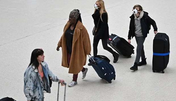 Travellers wearing protective face masks pull their suitcases while walking across the concourse at London Victoria train station in central London on March 3