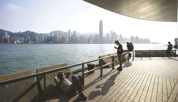 People relax on a Kowloon promenade that runs along Victoria Harbour, with the skyline of Hong Kong Island in the background yesterday. Hong Kongu2019s strict coronavirus containment measures are causing growing anxiety within the cityu2019s financial sector, after an outbreak forced several firms to shut offices and left some employees and their children stuck in spartan government quarantine facilities.