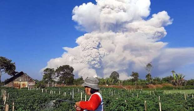 A farmer tends to a farm as Mount Sinabung spews ash into the sky, as seen from Karo, North Sumatra