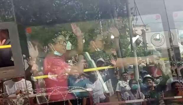 Onlookers are reflected off the windows as anti-coup demonstrators gesture from the bus after being released from Insein prison in Yangon, Myanmar