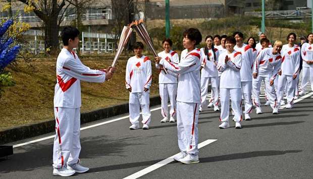 Japanese torchbearer Azusa Iwashimizu (front R), a member of the Japan women's national football team, passes the Olympic flame to high school student Asato Owada at a torch ,kiss point, during the torch relay grand start at the J-Village National Training Centre in Naraha town, Fukushima