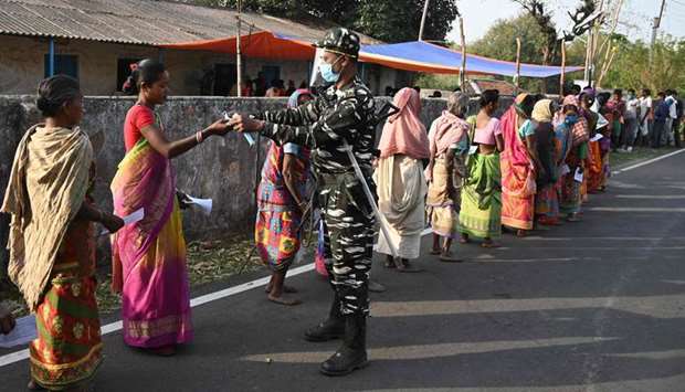 A paramilitary personnel distributes facemasks to voters standing in queue to cast their ballots outside a polling station during Phase 1 of West Bengal's legislative election in Purulia district