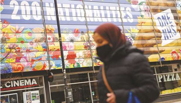 A woman wearing a face mask walks past an NHS-themed artwork on the side of a cinema in Shoreditch, London.