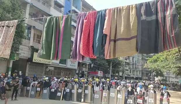 Traditional clothes hang on a rope as protesters holding shields stand in line in the background during a protest against the military coup in Yangon, Myanmar yesterday.