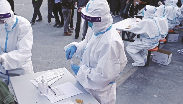 A medical worker in protective suit collects a swab from a resident at a makeshift nucleic acid testing site, following cases of Covid-19 in Shanghai, China.