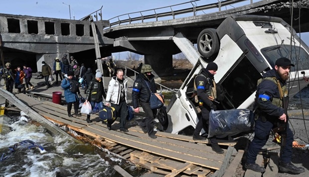 Ukrainian police officers help residents to cross a destroyed bridge as they evacuate Irpin, northwest of Kyiv, on March 12. AFP