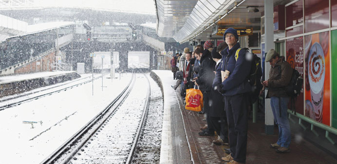 Commuters wait for trains during falling snow at East Croydon train station yesterday.