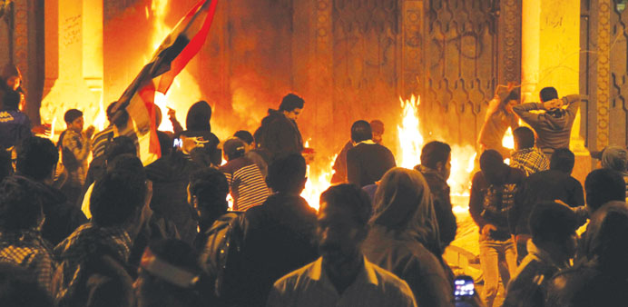 Protesters stand near flames at one of the gates of the presidential palace in Cairo yesterday.