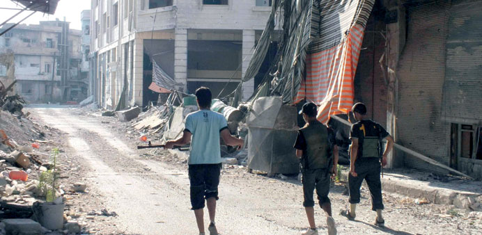 Members of the Free Syrian Army walk along a damaged street filled with debris in the besieged area of Homs yesterday.
