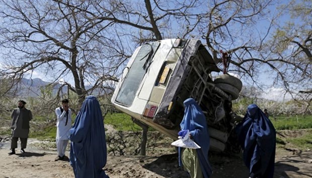 Women walk past a damaged mini-bus after it was hit by a bomb blast in the Bagrami district of Kabul on Monday.