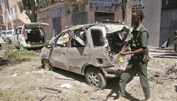 A Somali policeman walks to secure the wreckage of a car destroyed in a bomb explosion at a local government headquarters in Mogadishu.