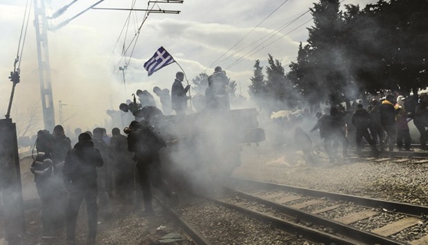 Refugees and migrants protest as a tear gas canister, fired on Sunday, exploded yesterday near their makeshift camp in the northern Greek border village of Idomeni.