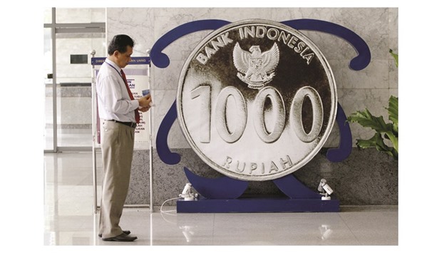 An employee of Bank Indonesia stands next to a giant one thousand rupiah coin on display inside the banku2019s headquarters in Jakarta. A new chat group on the instant messaging phone application WhatsApp is helping Indonesiau2019s central bank improve its reputation for managing market expectations, something it has struggled with in the past.