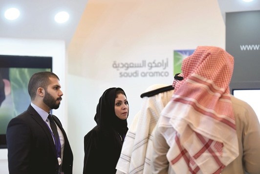 Saudi and foreign investors stand in front of the logo of Saudi state oil giant Aramco during the 10th Global Competitiveness Forum on January 25 in Riyadh. Fitch downgraded the kingdomu2019s credit rating to AA- from AA, and said the outlook remains negative, indicating a further cut is likely.