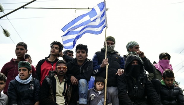 Refugees and migrants gather near the border with a Greek flag