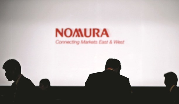 Investors stand in front of a screen showing the logo of Nomura Holdings in Tokyo. The Japanese firm  tries to stem losses incurred in its long-term drive to become a major global industry player by exiting European equity operations.
