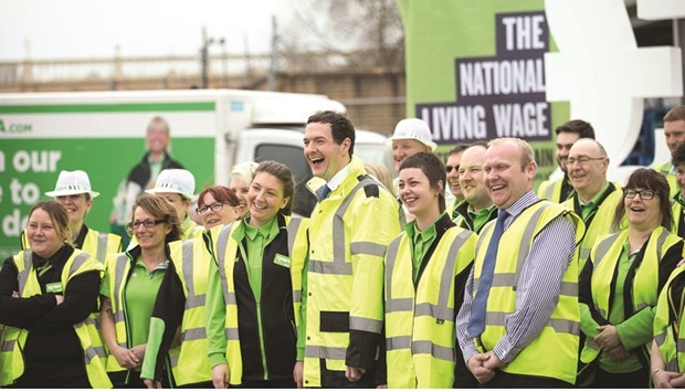 Finance Minister George Osborne poses with workers in the loading bay of an Asda supermarket in Manchester. The government raised the minimum wage by 7.5% yesterday in a move denounced by critics as largely symbolic.