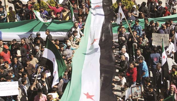 Protesters carry banners and opposition flags as they stand along a street during an anti-government protest in the rebel-controlled area of Maaret al-Numan town in Idlib province, Syria yesterday.