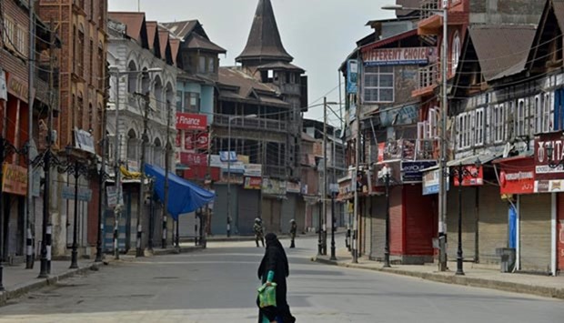 A woman walks on empty streets as paramilitary troops stand guard during a tense curfew in Srinagar on Friday
