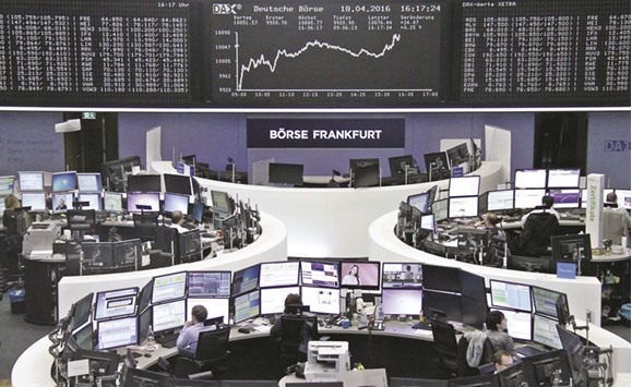 Traders work at their desks in front of the German share price index, DAX board, at the stock exchange in Frankfurt yesterday. European stocks turned moderately higher yesterday despite oil prices slipping after the worldu2019s top producers failed to reach a deal on freezing output in weekend talks in Doha.