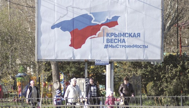 Locals walk past a billboard that promotes the construction of a bridge across the Kerch Strait to the Krasnodar region on a street in Kerch, Crimea. The board reads u201cCrimean spring. We build bridgesu201d.