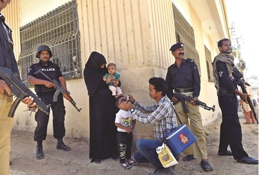 A Pakistani policeman stand guard as a health worker administers polio drops to a child during a polio vaccination campaign a day after an attack by gunmen in Karachi yesterday. Gunmen on motorcycle on Wednesday shot dead seven policemen guarding a polio vaccination team in Karachi, officials said.