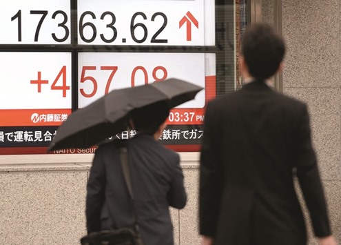 Businessmen walk past the electronic stock indicator outside a security company in Tokyo.  The benchmark Nikkei 225 index soared 457.08 points, to close at 17,363.62 yesterday.