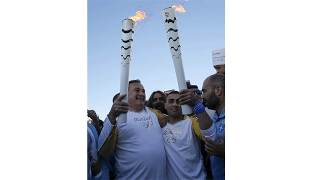 President of the Hellenic Olympic Committee Spiros Kapralos (L) hands over the Olympic Flame to Syrian refugee Ibrahim al-Hussein (2nd R), an amputee swimmer, during the Olympic Flame torch relay at the Eleonas refugee camp in Athens.