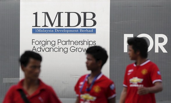 Pedestrians walk past a 1MDB billboard in Kuala Lumpur. The fund yesterday released a statement saying it was u2018now in defaultu2019 on the bonds after missing the $50mn interest payment.