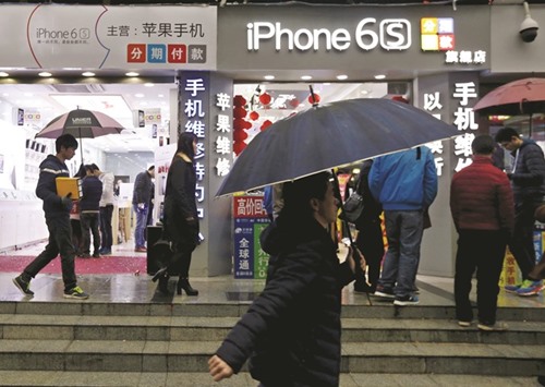 People walk past stores promoting the Apple iPhone 6S in the southern city of Shenzhen, China. The companyu2019s shares sank 7.2% yesterday after its second-quarter earnings showed a fall in profit.