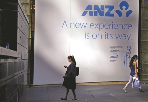 A woman looks at her iPhone as she walks past a signboard announcing a new branch of the Australia and New Zealand Banking Group in central Sydney. Apple expanded its Apple Pay digital wallet in Australia yesterday after ANZ became the countryu2019s first bank to support the mobile payment service, executives said.