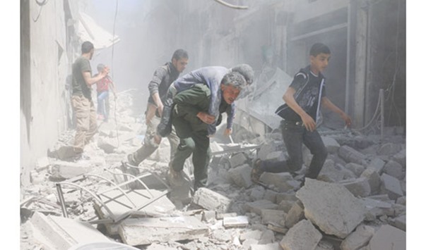 Syrians evacuate an injured man amid the rubble of destroyed buildings following a reported air strike on the rebel-held neighbourhood of Al Qatarji, in Aleppo yesterday.