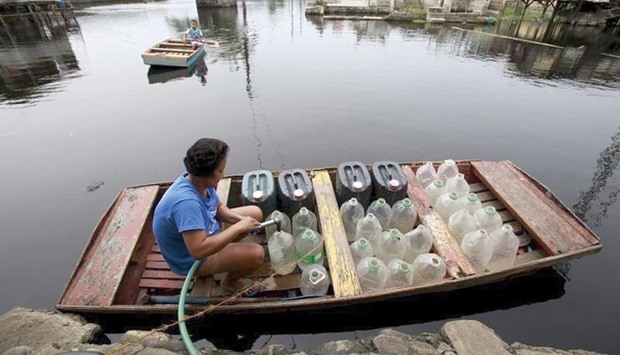 A resident living in a flooded area refills plastic containers with drinking water on an improvised u201cbancau201d (small boat) in Artex compound, Malabon city, north of Manila, in March this year.