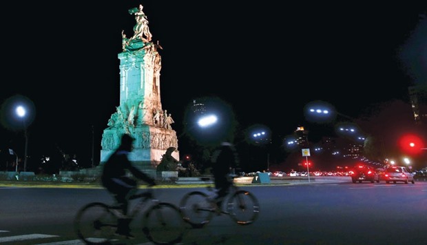 Two men riding their bicycles in front of the Monument to the Spanish, lit in the colours of Brazilu2019s flag in celebration of the 100 days before the 2016 Rio Olympics, in Buenos Aires, Argentina.  Latin America could eventually replace Europe as the world region that others regard with more than a little admiration, or even envy, if  current trends persist.