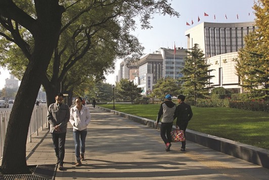 Pedestrians walk past the Peopleu2019s Bank Of China headquarters (right) in Beijing. The PBoC has lowered benchmark interest rates six times since 2014, helping fuel an advance in the bond market and driving debt to a record 247% of gross domestic product in 2015.