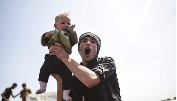 A man holds up a child as migrants and refugees protest for the opening of the border gate at their makeshift camp near the northern Greek border village of Idomeni.