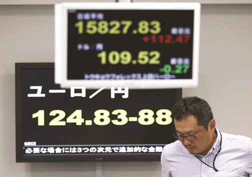 An employee of a foreign currency company is seen next to an electronic screen  displaying Japanu2019s Nikkei average (top), the exchange rate between Japanese yen against the US dollar and euro (bottom) at a dealing room in Tokyo.