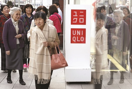 Pedestrians walk past logos of Fast Retailingu2019s Uniqlo outside its store in Tokyo. The firm now illustrates a bleaker picture of a corporate sector squeezed by sticky overhead costs, cooling consumer enthusiasm and lower prices.