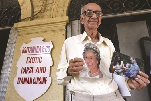 Boman Kohinoor, 93, poses with photos of Queen Elizabeth, and the Duke and Duchess of Cambridge outside the Britannia & Co restaurant.