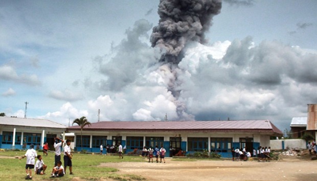 Indonesian pupils playing with the background of Mount Sinabung volcano spewing thick smoke in Karo, North Sumatra.